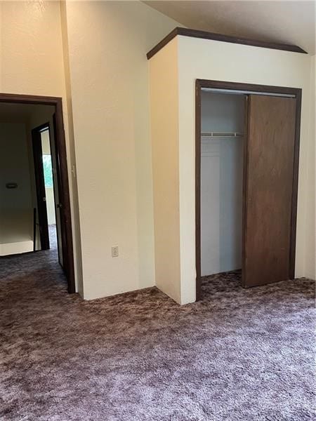 unfurnished bedroom with a closet, dark carpet, and lofted ceiling