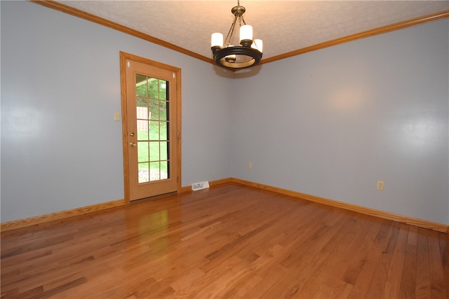 spare room with a wealth of natural light, an inviting chandelier, hardwood / wood-style flooring, and ornamental molding