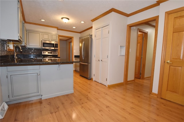 kitchen with kitchen peninsula, stainless steel appliances, light hardwood / wood-style floors, tasteful backsplash, and sink