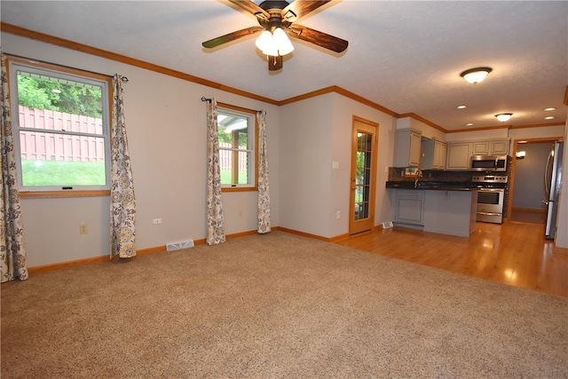 interior space featuring ornamental molding, light colored carpet, stainless steel appliances, and ceiling fan