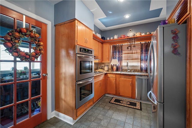 kitchen featuring light stone counters, appliances with stainless steel finishes, sink, dark tile flooring, and backsplash