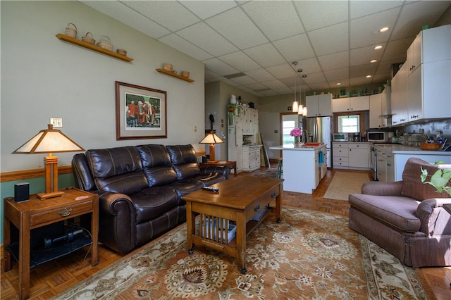 living room with a drop ceiling and light parquet flooring