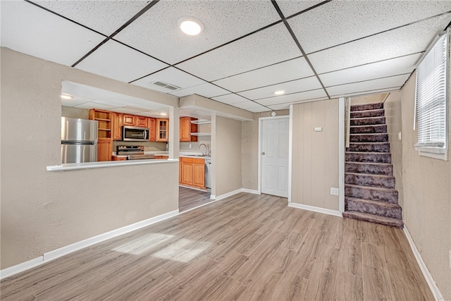 unfurnished living room featuring sink, light hardwood / wood-style flooring, and a paneled ceiling