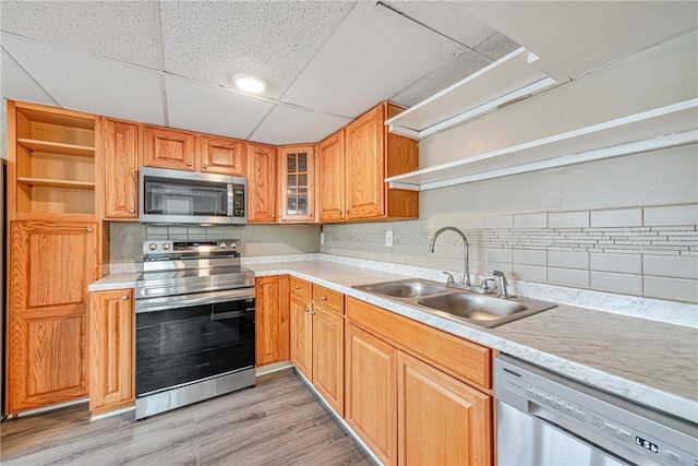 kitchen with a paneled ceiling, backsplash, light wood-type flooring, appliances with stainless steel finishes, and sink