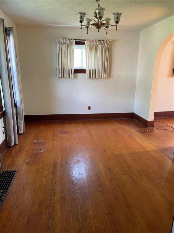 empty room with hardwood / wood-style floors, a textured ceiling, and a chandelier