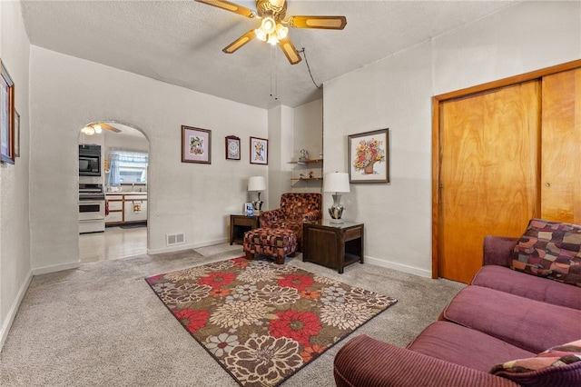 living room featuring ceiling fan, carpet flooring, and a textured ceiling