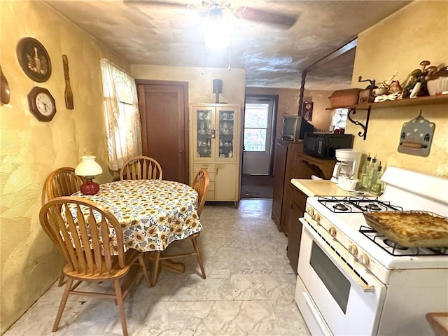 kitchen featuring white gas range oven, ceiling fan, and light tile floors