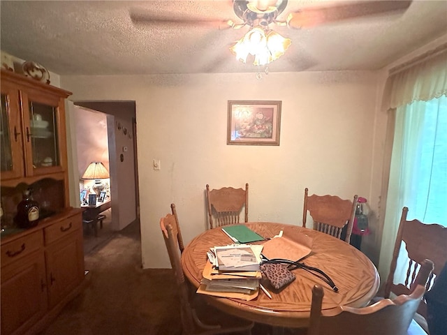 dining room featuring dark carpet, ceiling fan, and a textured ceiling