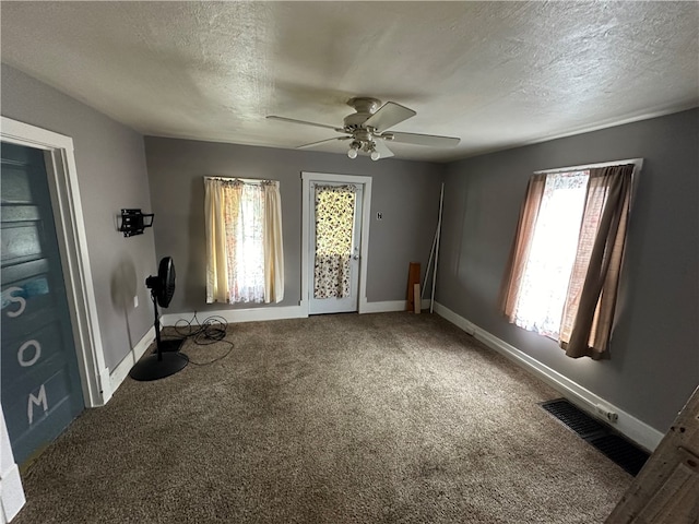 spare room with ceiling fan, dark colored carpet, and a healthy amount of sunlight