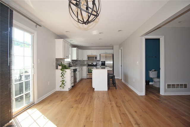 kitchen featuring white cabinetry, a kitchen island, light wood-type flooring, appliances with stainless steel finishes, and tasteful backsplash