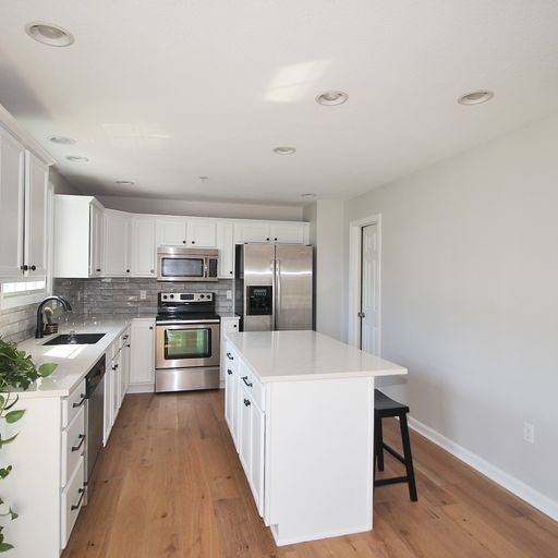 kitchen featuring stainless steel appliances, a kitchen island, sink, hardwood / wood-style flooring, and white cabinetry