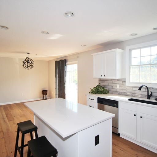 kitchen with white cabinetry, a kitchen island, light hardwood / wood-style flooring, stainless steel dishwasher, and sink