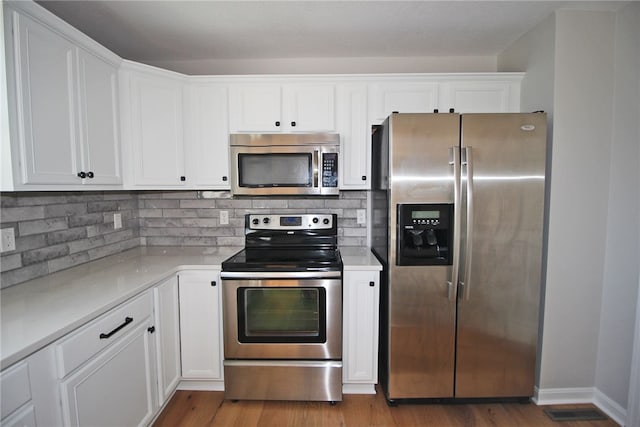 kitchen featuring stainless steel appliances, white cabinetry, hardwood / wood-style flooring, and backsplash