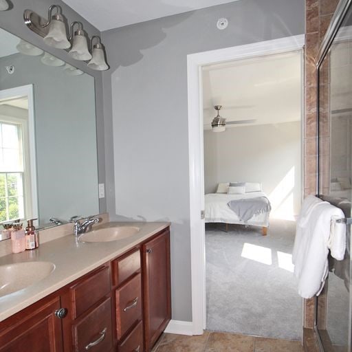 bathroom featuring a shower with door, double vanity, tile flooring, and ceiling fan