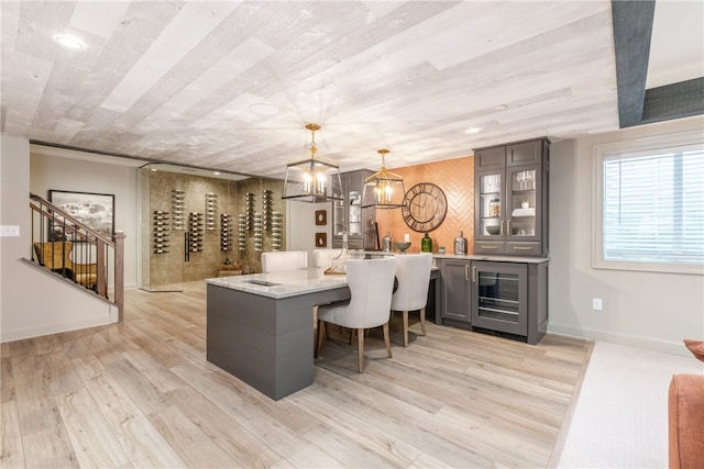 kitchen featuring decorative light fixtures, light hardwood / wood-style floors, beverage cooler, a notable chandelier, and a kitchen breakfast bar