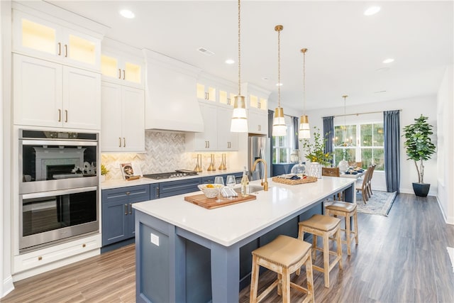 kitchen with custom range hood, stainless steel appliances, backsplash, hanging light fixtures, and hardwood / wood-style floors