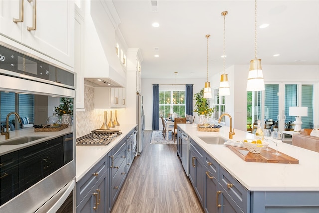 kitchen with light hardwood / wood-style floors, pendant lighting, custom range hood, sink, and white cabinets