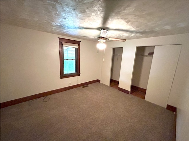 unfurnished bedroom with multiple closets, dark colored carpet, and ceiling fan