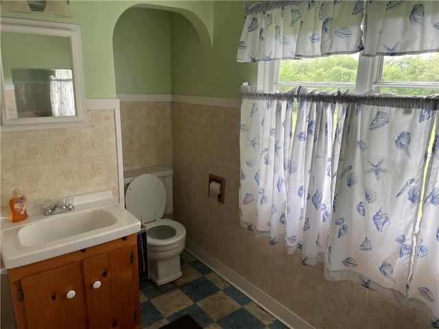 bathroom with tile floors, large vanity, toilet, and tile walls