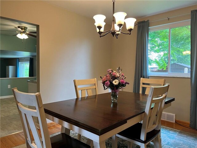 dining space with ceiling fan with notable chandelier, hardwood / wood-style flooring, and plenty of natural light