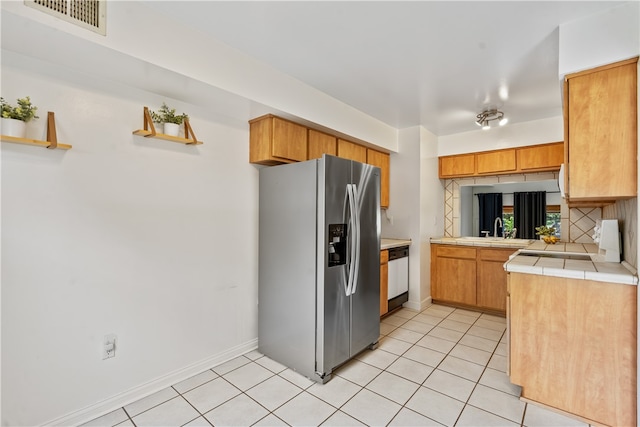 kitchen featuring tasteful backsplash, light tile floors, sink, stainless steel fridge with ice dispenser, and tile countertops