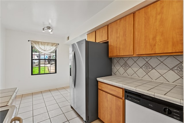 kitchen featuring white dishwasher, tile counters, backsplash, stainless steel refrigerator with ice dispenser, and light tile floors