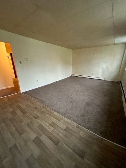 unfurnished room with wood-type flooring, baseboard heating, and a paneled ceiling