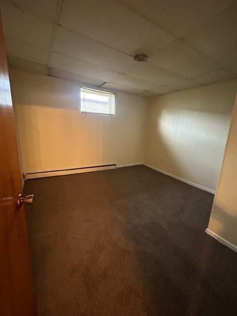 spare room with a paneled ceiling, a baseboard radiator, and dark colored carpet