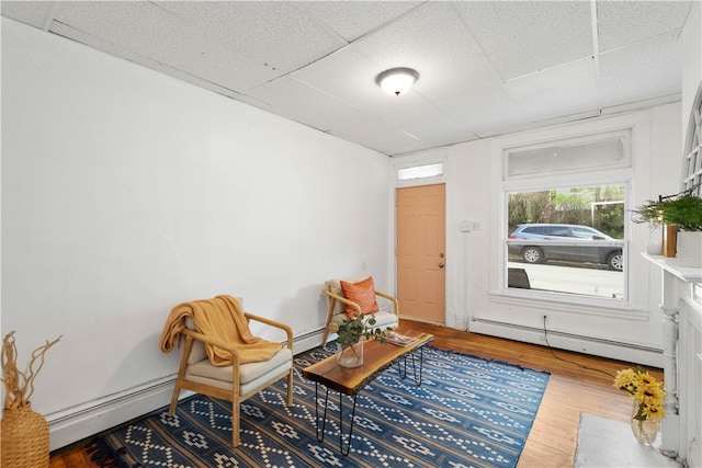 sitting room featuring wood-type flooring, baseboard heating, and a paneled ceiling