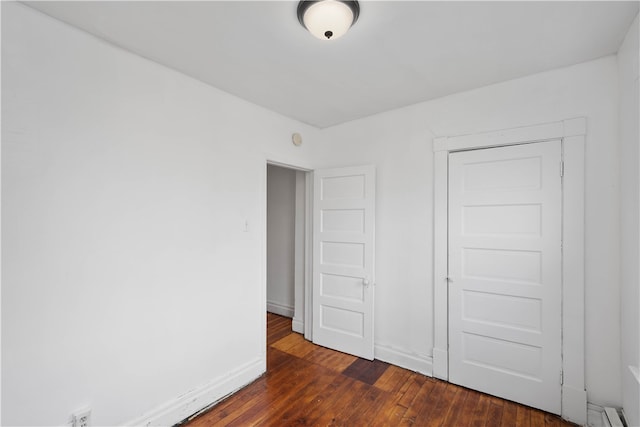 unfurnished bedroom with a closet, a baseboard radiator, and dark wood-type flooring