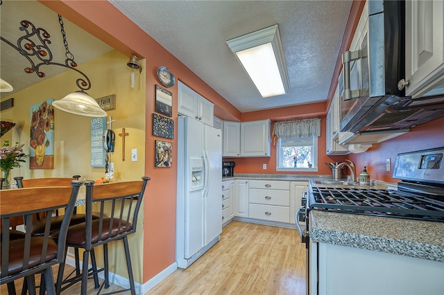 kitchen with gas range oven, decorative light fixtures, light hardwood / wood-style floors, white refrigerator with ice dispenser, and white cabinets