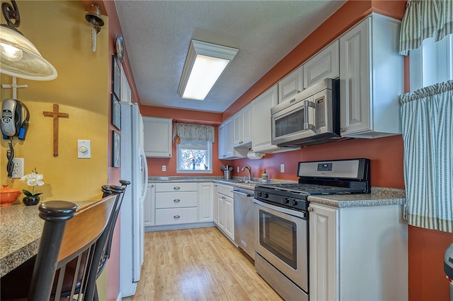 kitchen featuring stainless steel appliances, light wood-type flooring, a textured ceiling, sink, and white cabinetry