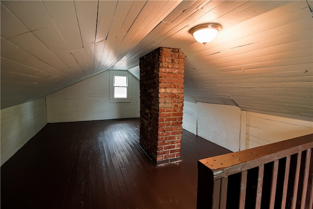 bonus room with dark hardwood / wood-style floors, lofted ceiling, and brick wall