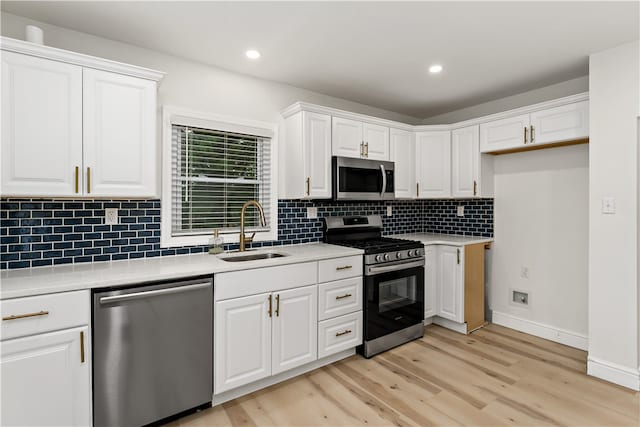 kitchen with light wood-type flooring, backsplash, sink, white cabinetry, and appliances with stainless steel finishes