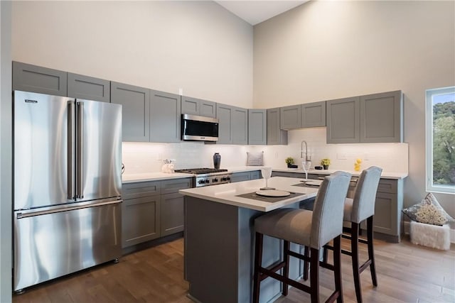 kitchen with gray cabinets, a kitchen island, a towering ceiling, a breakfast bar area, and stainless steel appliances