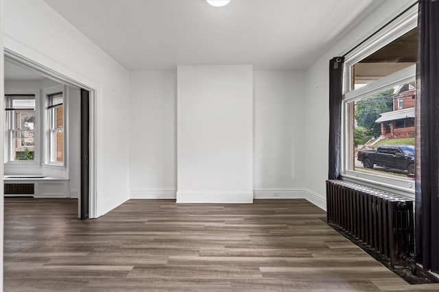 empty room with dark wood-type flooring, plenty of natural light, and radiator