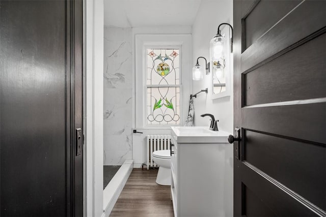 bathroom featuring hardwood / wood-style flooring, radiator heating unit, a shower, vanity, and toilet