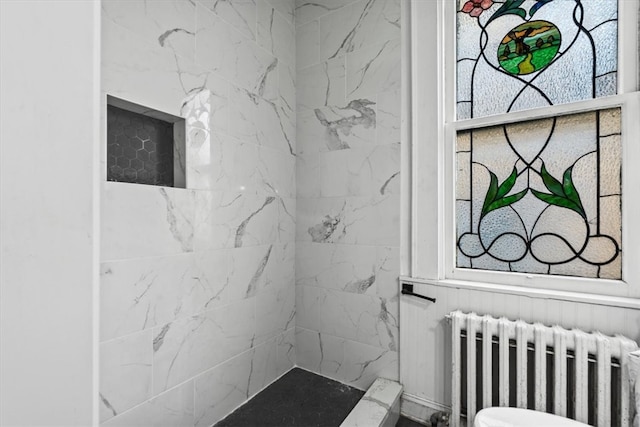 bathroom featuring a tile shower, radiator heating unit, and toilet