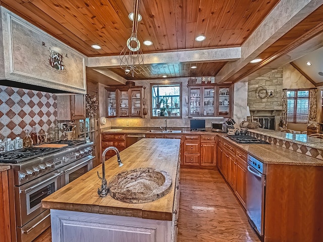 kitchen featuring stainless steel appliances, hardwood / wood-style flooring, a stone fireplace, an island with sink, and wood ceiling