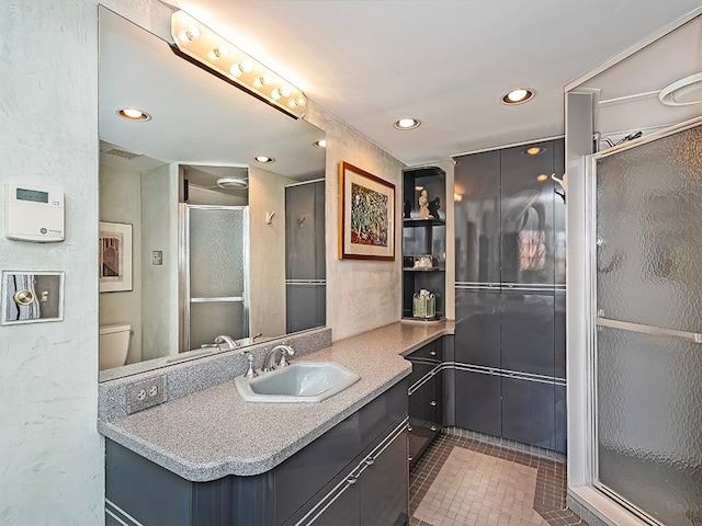 bathroom featuring tile floors, a shower with door, toilet, and vanity