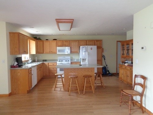 kitchen with light hardwood / wood-style flooring, a kitchen island, sink, white appliances, and a breakfast bar