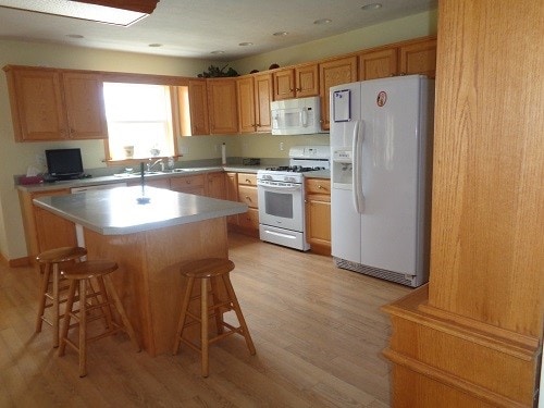 kitchen with a kitchen breakfast bar, white appliances, light wood-type flooring, a kitchen island, and sink