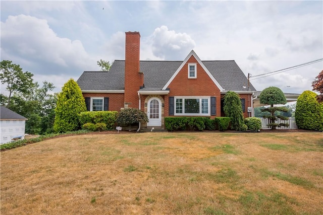 view of front of home featuring roof with shingles, brick siding, a chimney, and a front lawn