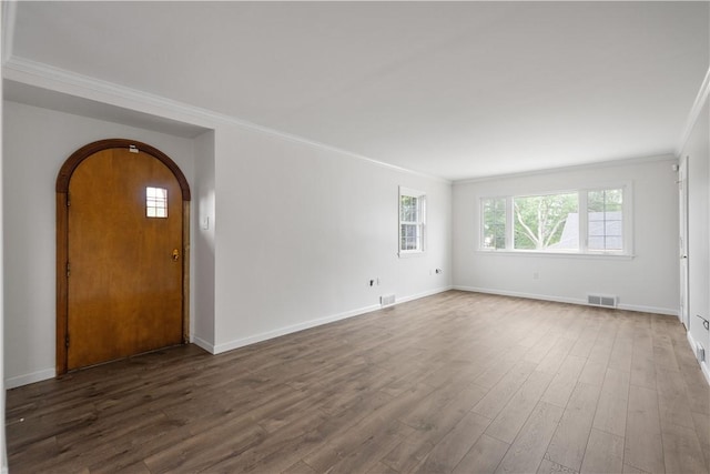 interior space featuring visible vents, arched walkways, baseboards, dark wood-style floors, and crown molding