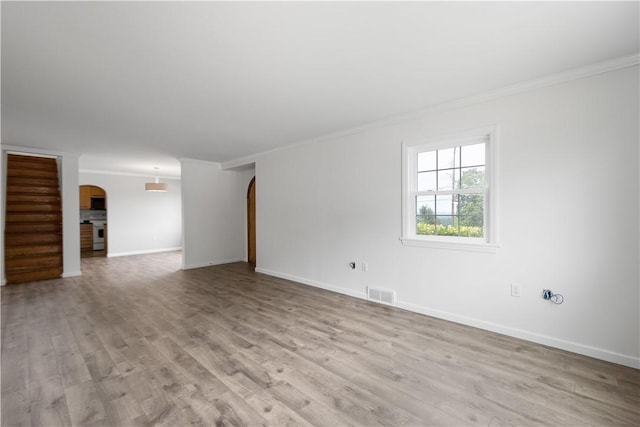 empty room featuring arched walkways, visible vents, ornamental molding, light wood-type flooring, and baseboards