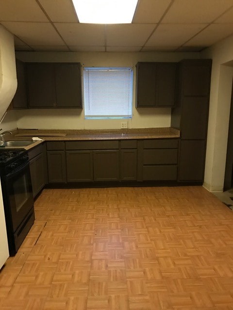 kitchen featuring black gas stove, sink, light parquet flooring, and a drop ceiling