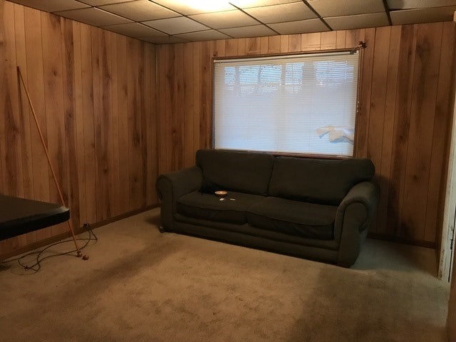 living room featuring wooden walls, carpet flooring, and a drop ceiling