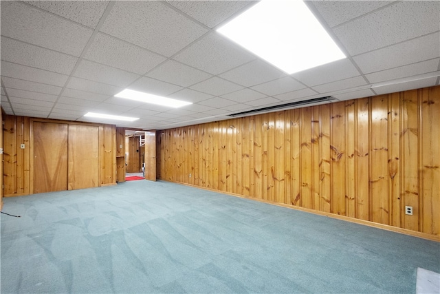 basement with wood walls, a drop ceiling, and carpet