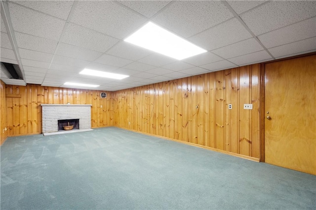 basement with carpet flooring, a drop ceiling, a fireplace, and wood walls