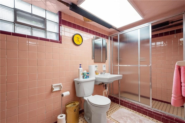 bathroom with toilet, a shower with shower door, sink, and tile walls